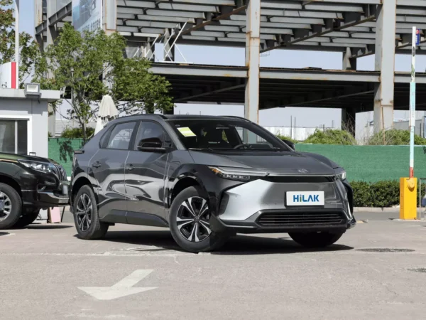 A close-up view of the front end of a gray Toyota BZ4X electric car with a parking lot entrance railing behind the car.