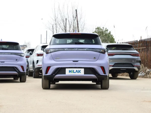 Rear view of a lavender BYD Dolphin electric car parked in a parking lot next to other vehicles.