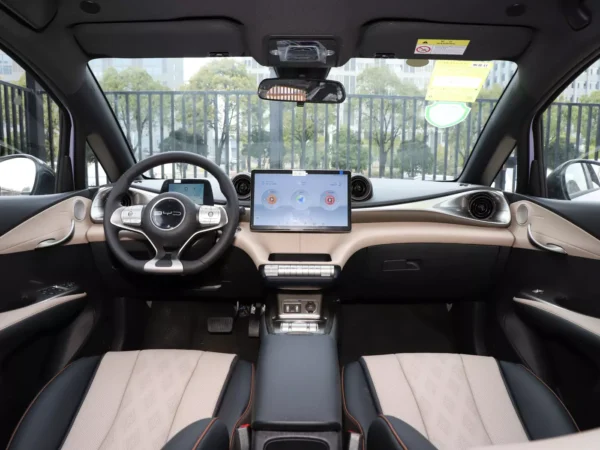 A close-up view of the interior cabin of the BYD Dolphin EV, which is very spacious, with a screen to the right of the steering wheel. The interior is cream and black.