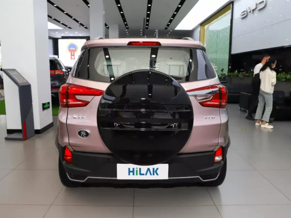 A close-up of the rear of a pink BYD Yuan Pro electric car with a black spare tire hanging off the car, next to two people observing the car.